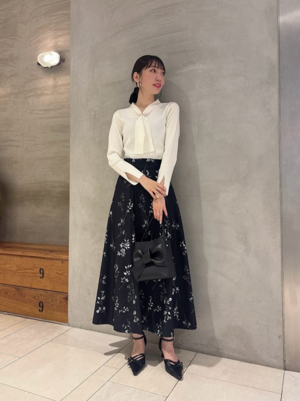 ブラック系のパンプス、ホワイト系のニット/セーター、ブラック系のスカートを着用したレディースの秋コーディネートの1枚目の写真