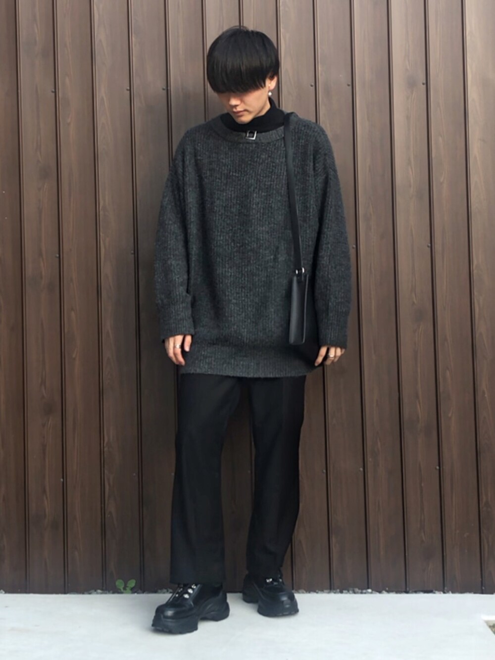 グレー系のニット/セーター、ブラック系のTシャツ/カットソー、ブラック系のスラックスを着用したメンズの秋コーディネートの1枚目の写真