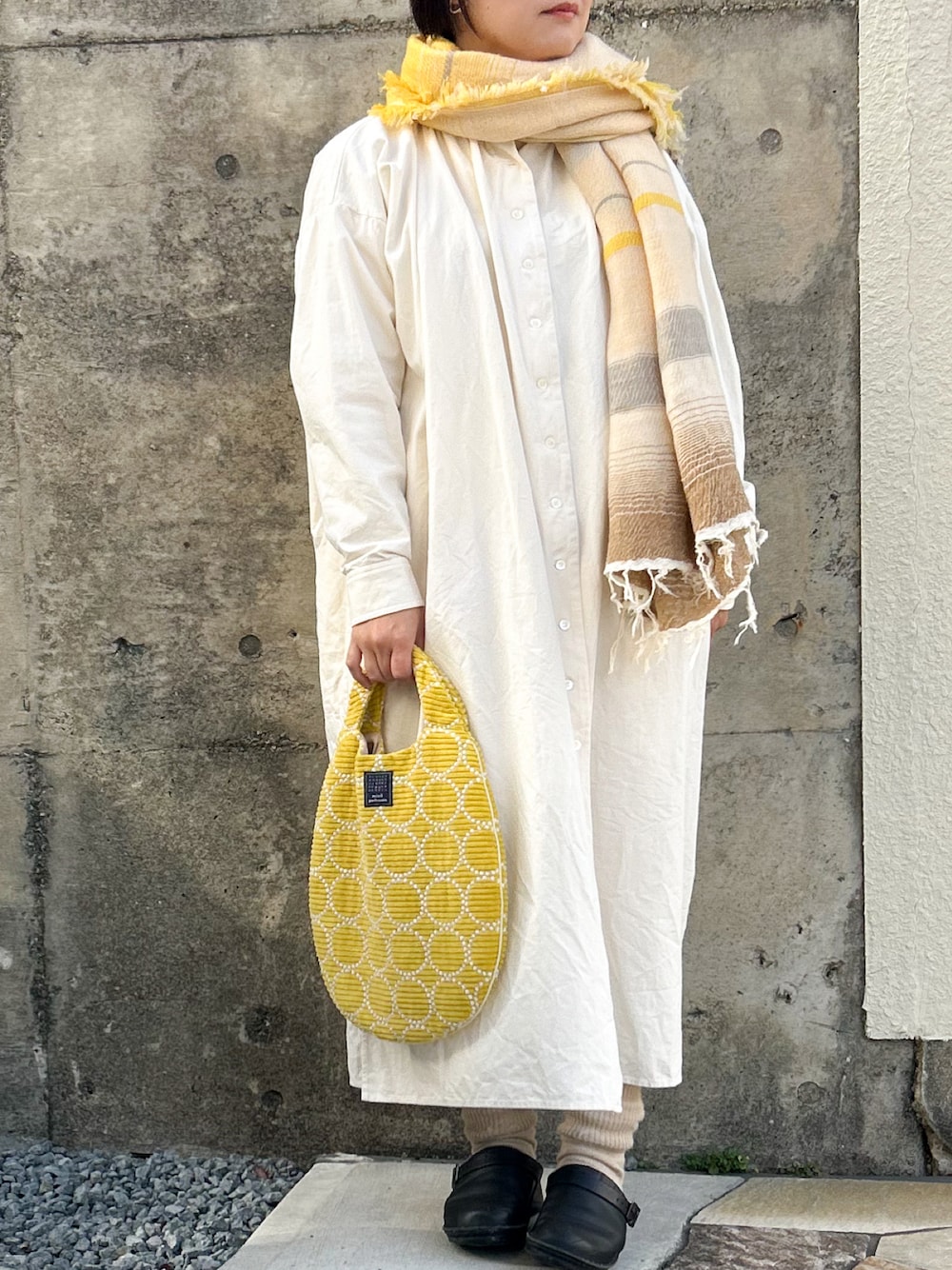 イエロー系のハンドバッグ、ブラック系のスリッポン、ホワイト系のワンピース/ドレスを着用したレディースの冬コーディネートの1枚目の写真