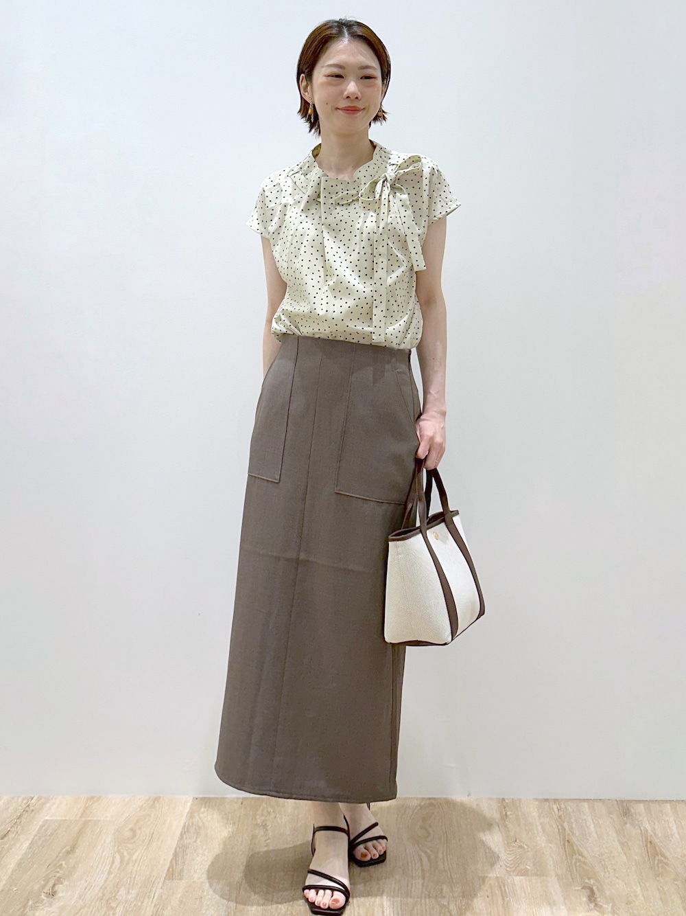 ベージュ系のシャツ/ブラウス、ブラウン系のスカート、ブラウン系のトートバッグを着用したレディースの夏コーディネートの1枚目の写真