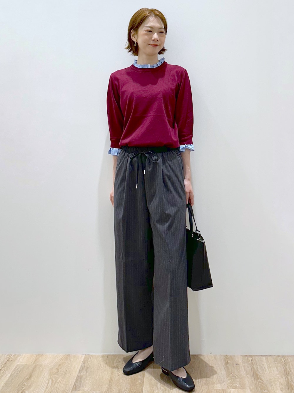 レッド系のニット/セーター、グレー系のその他パンツ、ブラック系のトートバッグを着用したレディースの秋コーディネートの1枚目の写真