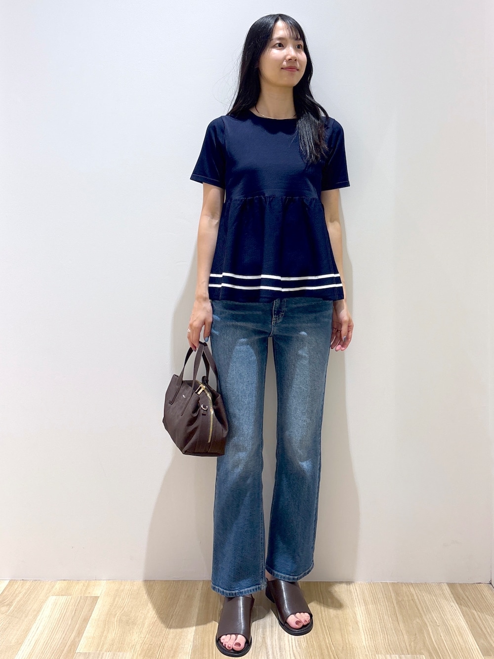 ブルー系のニット/セーター、ブルー系のデニムパンツ、ブラウン系のボストンバッグを着用したレディースの夏コーディネートの1枚目の写真