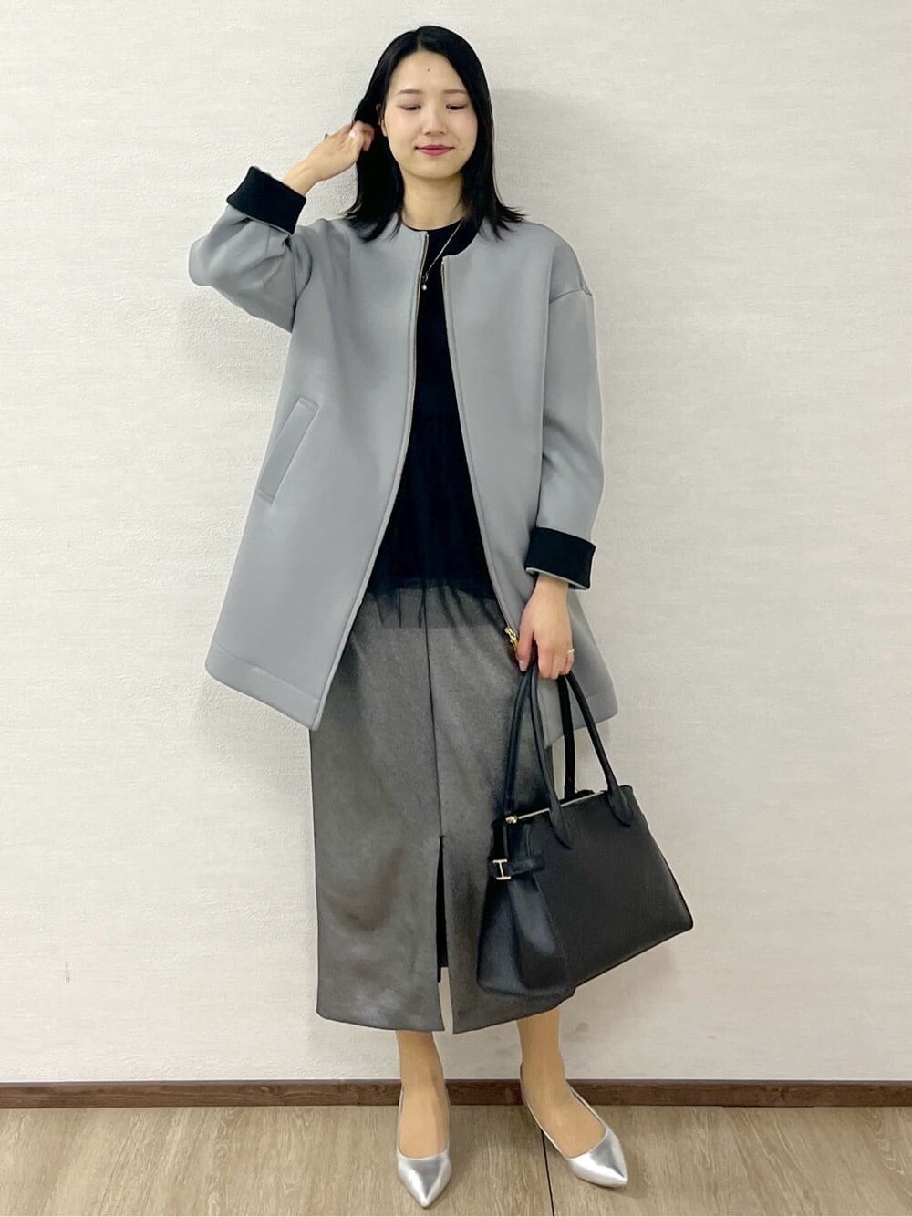 グレー系のノーカラーコート、ブラック系のTシャツ/カットソー、ブラック系のスカートを着用したレディースの冬コーディネートの1枚目の写真