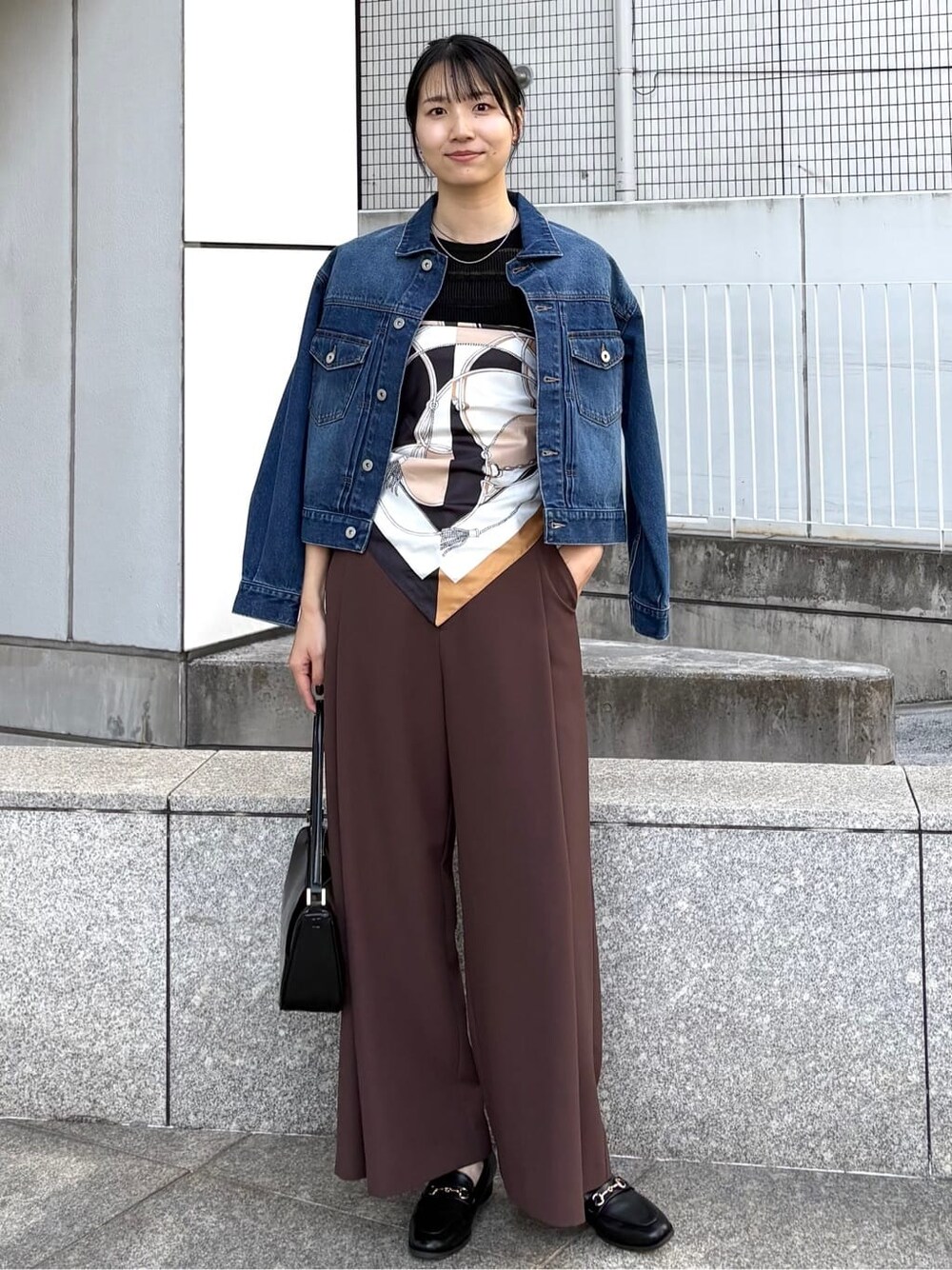 ブルー系のデニムジャケット、ブラック系のニット/セーター、ブラック系のショルダーバッグを着用したレディースの春コーディネートの1枚目の写真