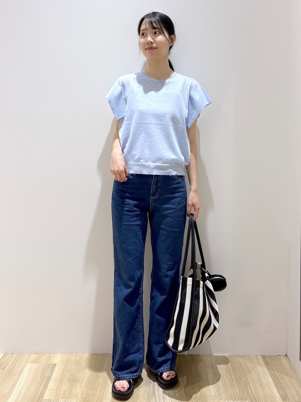 ブルー系のニット/セーター、ブルー系のデニムパンツ、ブラック系のトートバッグを着用したレディースの夏コーディネートの1枚目の写真