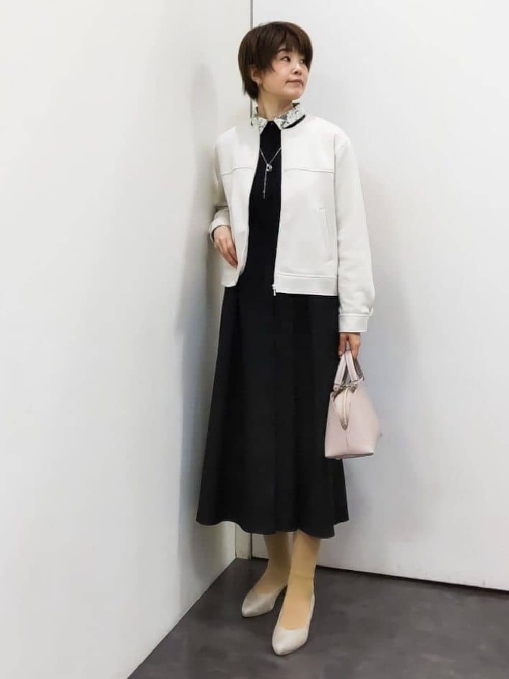 ホワイト系のノーカラージャケット、ブラック系のワンピース、ピンク系のハンドバッグを着用したレディースの冬コーディネートの1枚目の写真