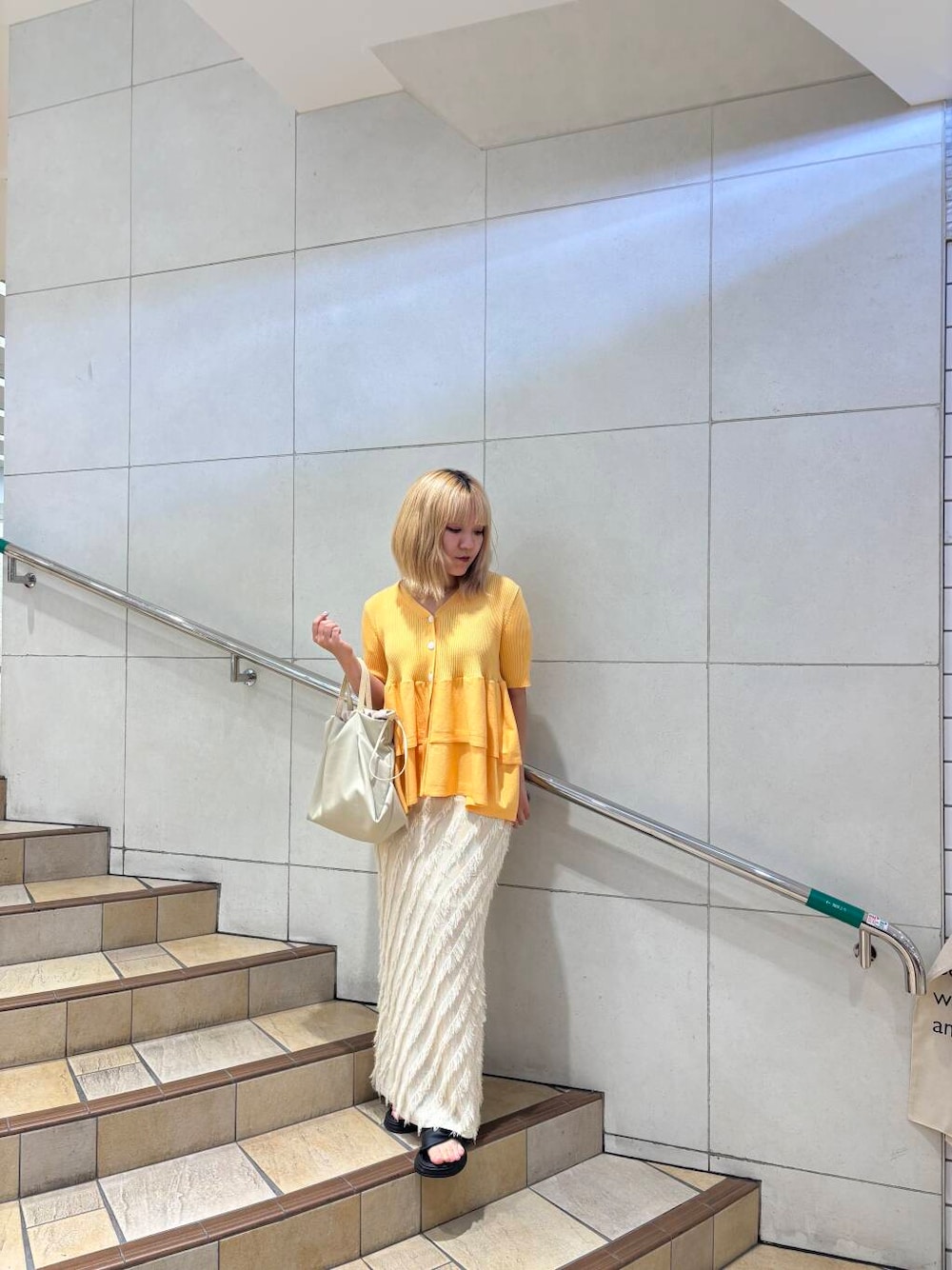 オレンジ系のカーディガン/ボレロ、ベージュ系のスカート、ホワイト系のショルダーバッグを着用したレディースの夏コーディネートの1枚目の写真