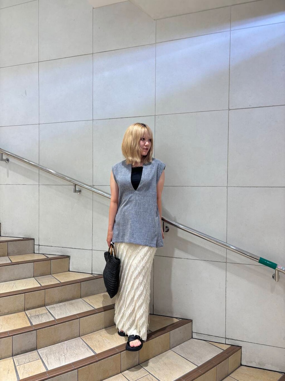 ブラック系のトートバッグ、ベージュ系のスカート、ブルー系のベストを着用したレディースの夏コーディネートの1枚目の写真