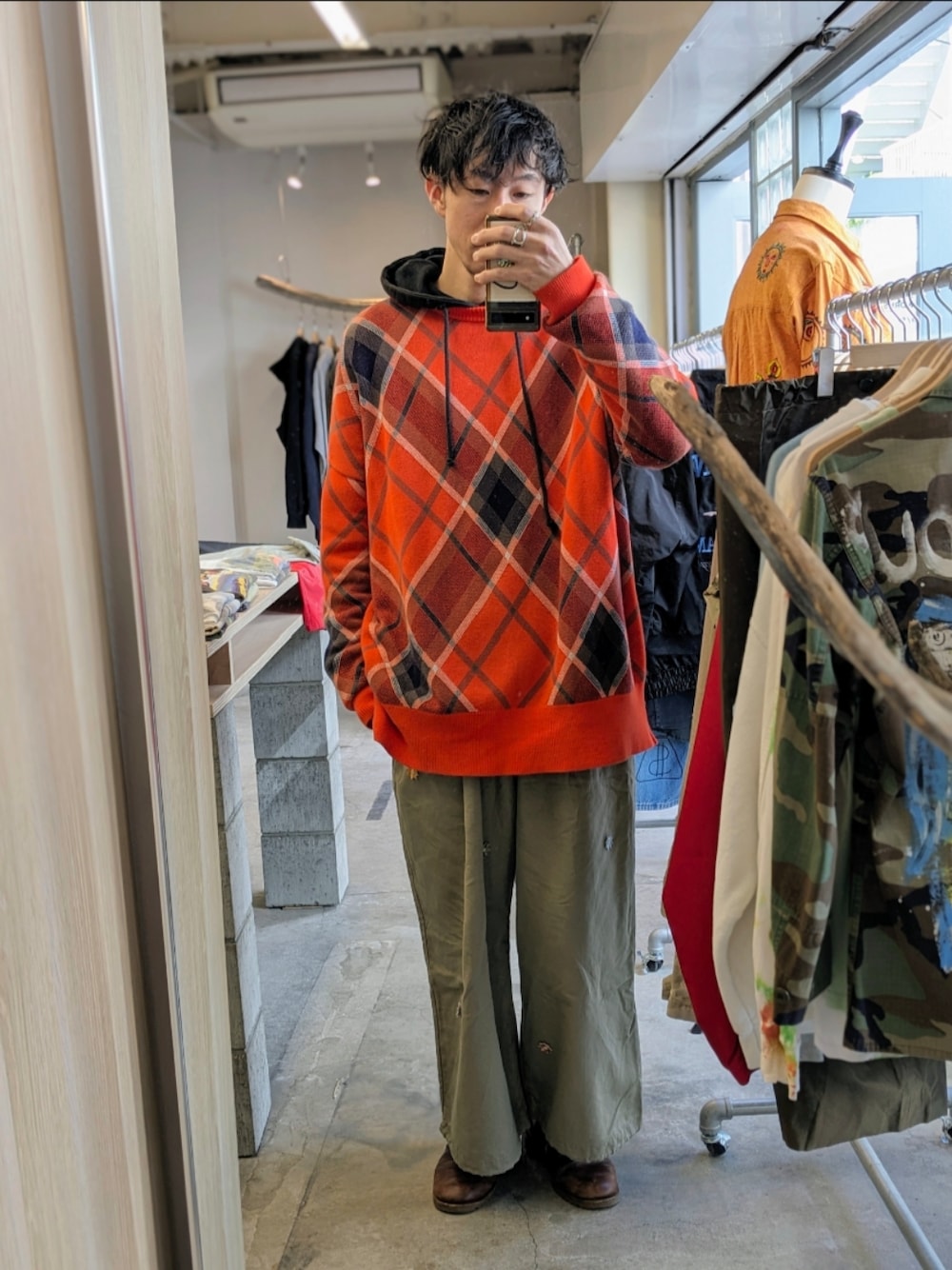 オレンジ系のニット/セーター、ベージュ系のチノパンツを着用したメンズの春コーディネートの1枚目の写真