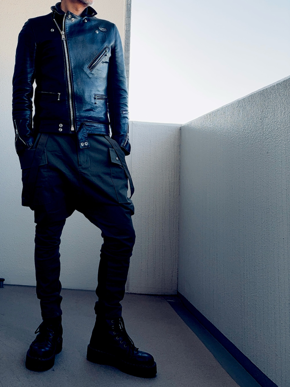 ブラック系のライダースジャケット、グリーン系のカーゴパンツ、ブラック系のブーツを着用したメンズの秋コーディネートの1枚目の写真