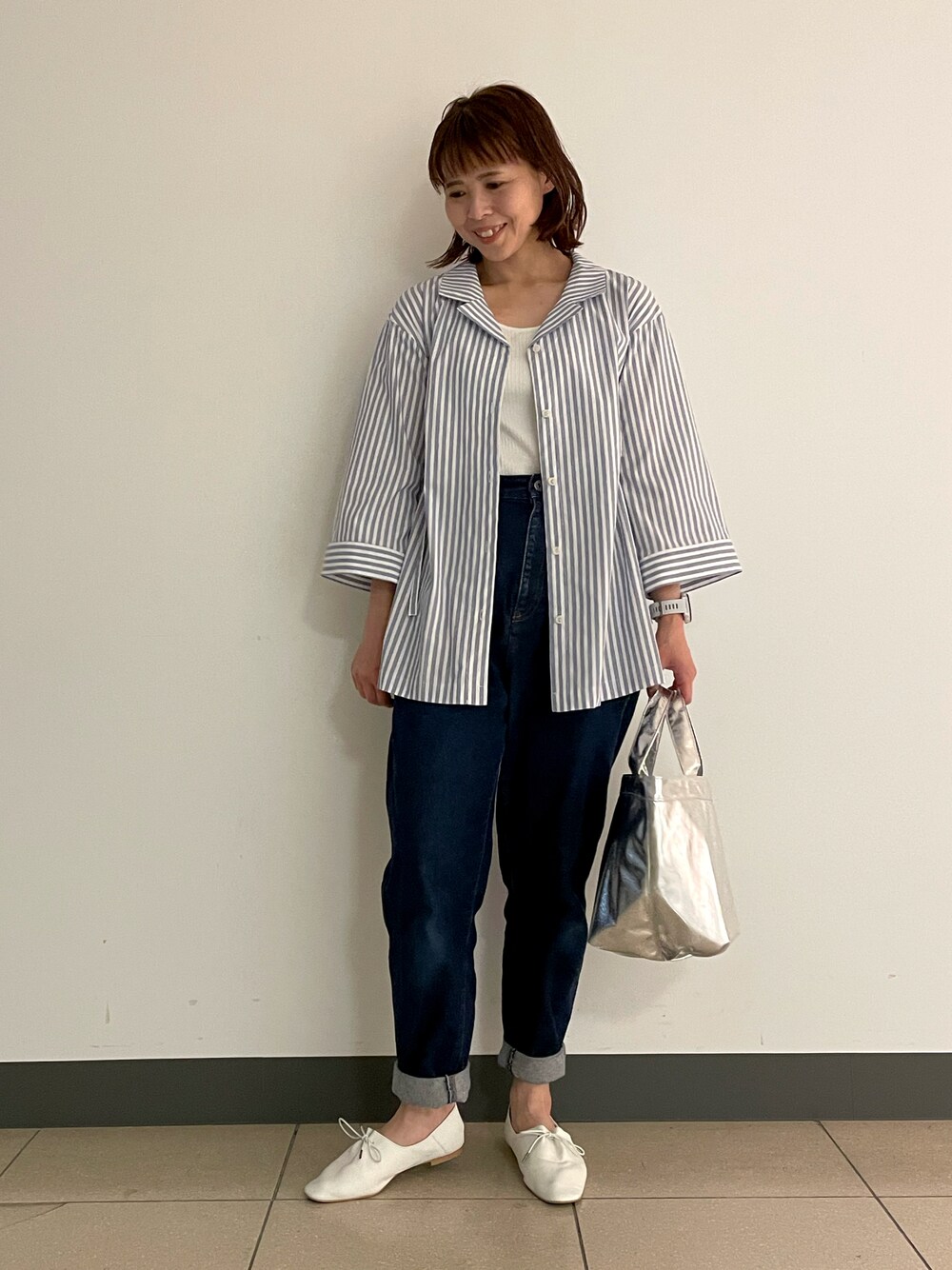 ブルー系のデニムパンツ、ホワイト系のドレスシューズ、シルバー系のトートバッグを着用したレディースの春コーディネートの1枚目の写真