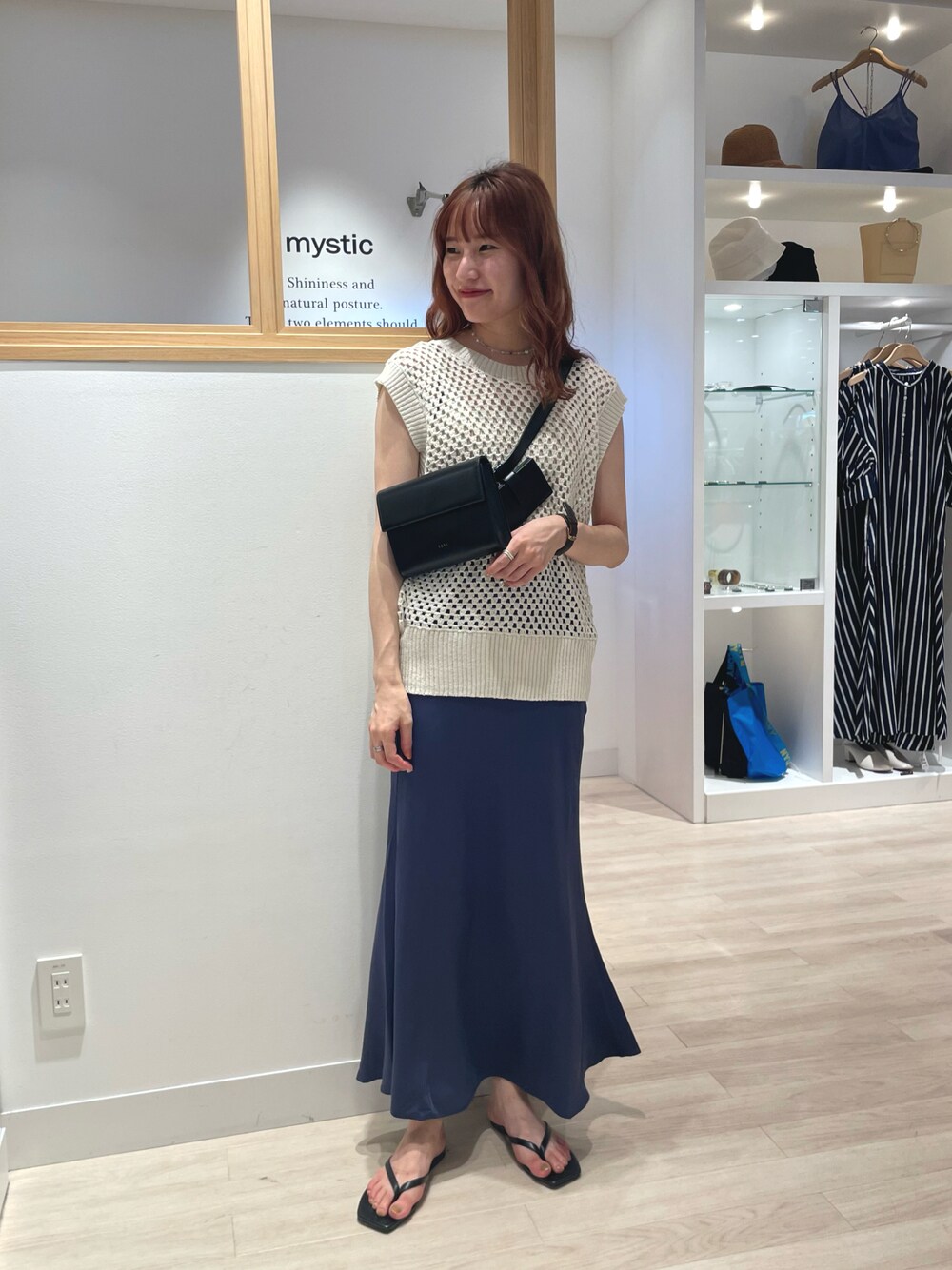 ホワイト系のベスト、ブルー系のスカート、ブラック系のショルダーバッグを着用したレディースの夏コーディネートの1枚目の写真