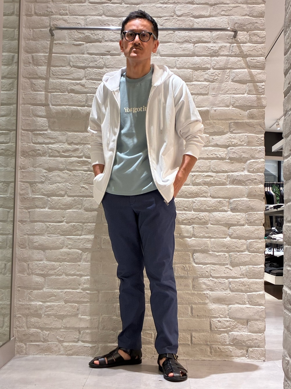 ホワイト系のパーカー、グリーン系のTシャツ/カットソー、ブルー系のスラックスを着用したメンズの春コーディネートの1枚目の写真
