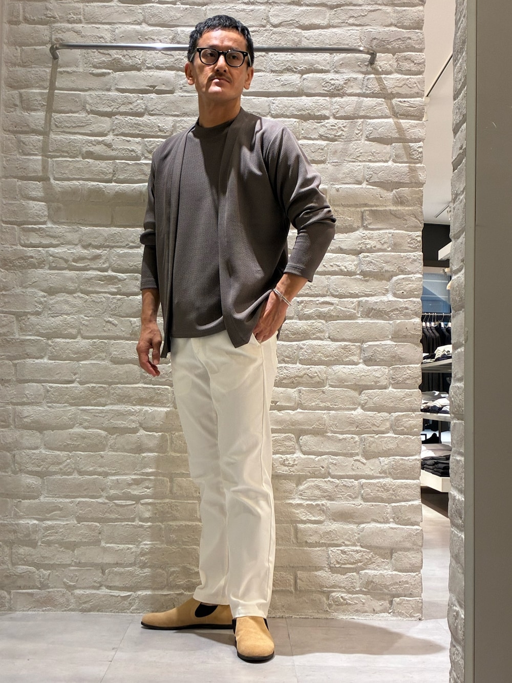 ブラウン系のカーディガン/ボレロ、ブラウン系のTシャツ/カットソー、ホワイト系のスラックスを着用したメンズの秋コーディネートの1枚目の写真