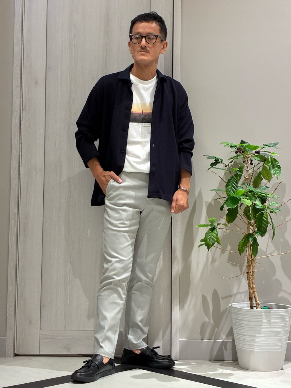 ブルー系のカーディガン/ボレロ、ホワイト系のTシャツ/カットソー、ベージュ系のスラックスを着用したメンズの秋コーディネートの1枚目の写真