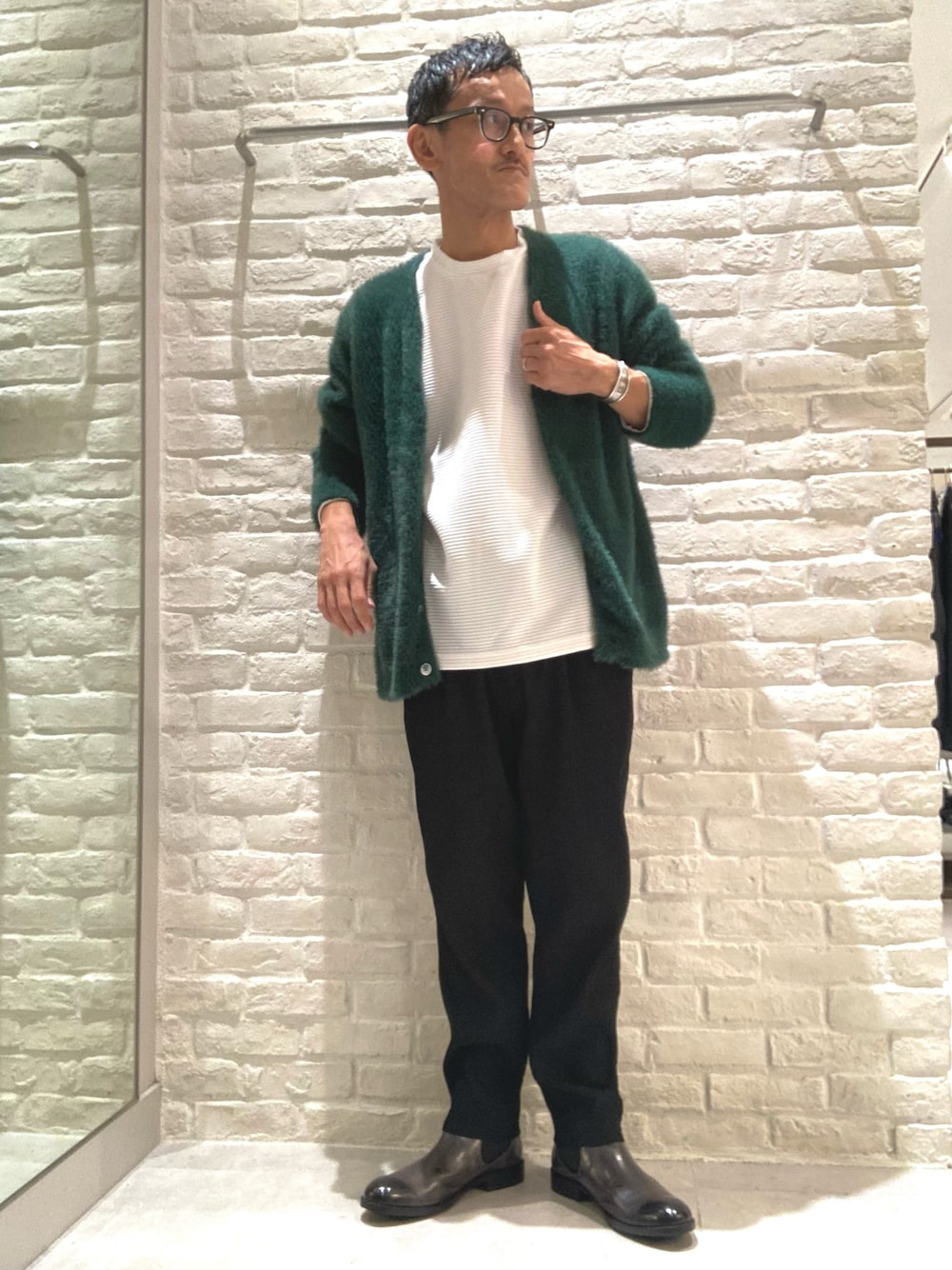 グリーン系のカーディガン/ボレロ、ホワイト系のTシャツ/カットソー、ブラック系のスラックスを着用したメンズの秋コーディネートの1枚目の写真