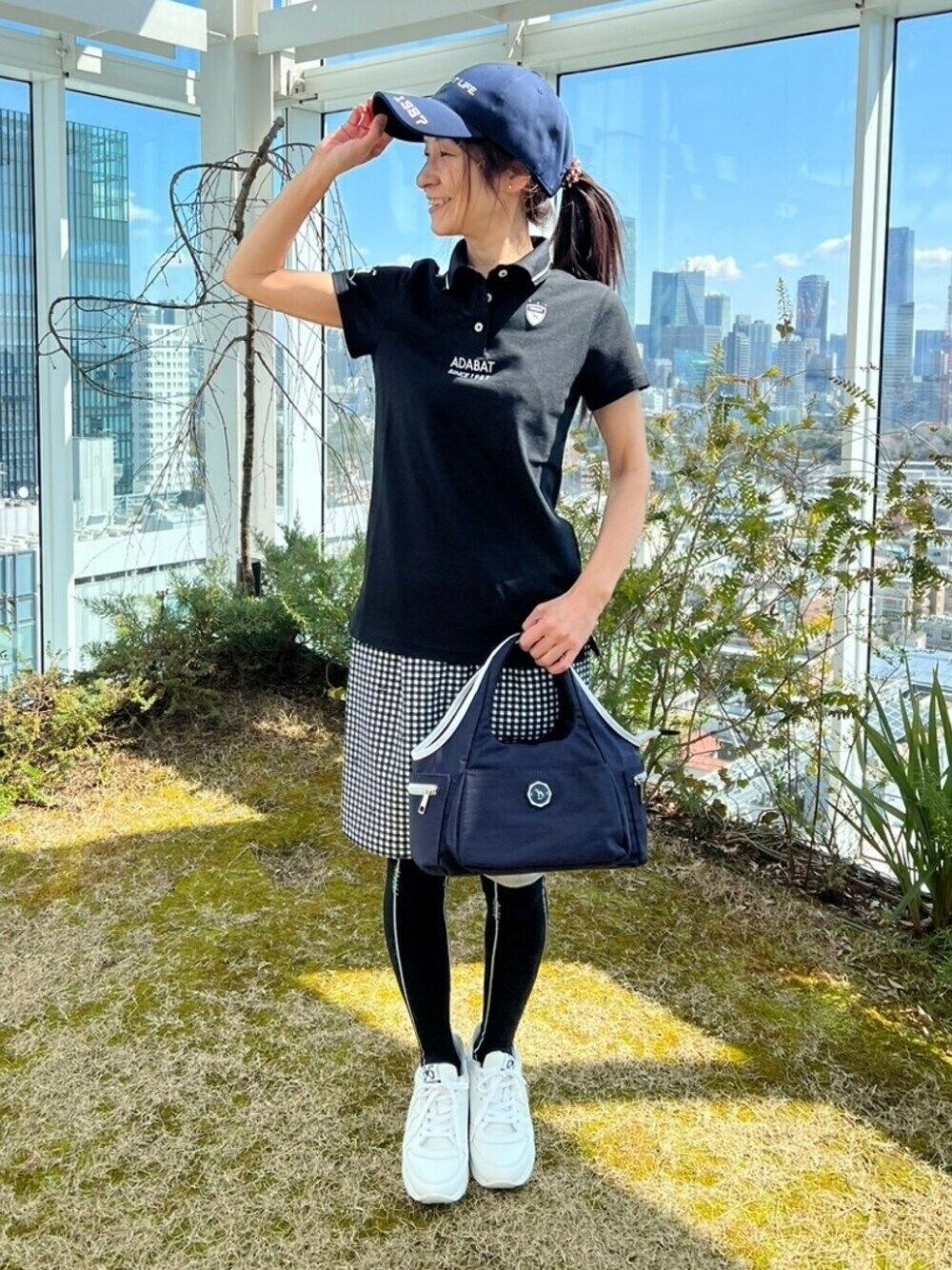 ブラック系のポロシャツ、ブルー系のハンドバッグ、ブルー系のスカートを着用したレディースの春コーディネートの1枚目の写真