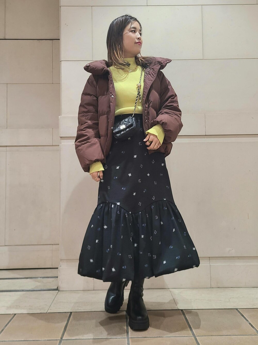 ブラウン系のダウンジャケット/コート、ブラック系のショルダーバッグ、イエロー系のニット/セーターを着用したレディースの冬コーディネートの1枚目の写真