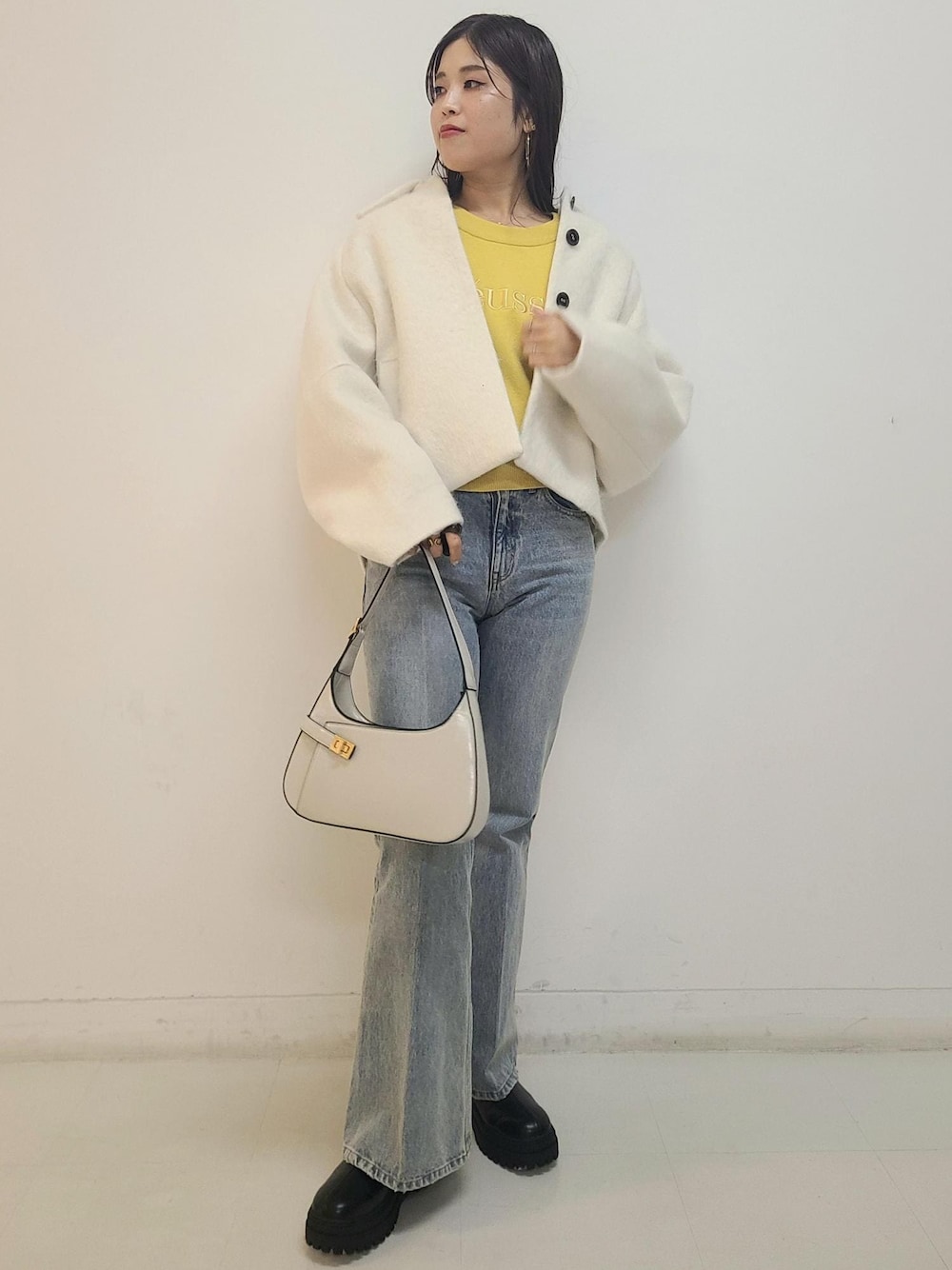 ブルー系のデニムパンツ、ブラック系のブーツ、ホワイト系のハンドバッグを着用したレディースの秋コーディネートの1枚目の写真