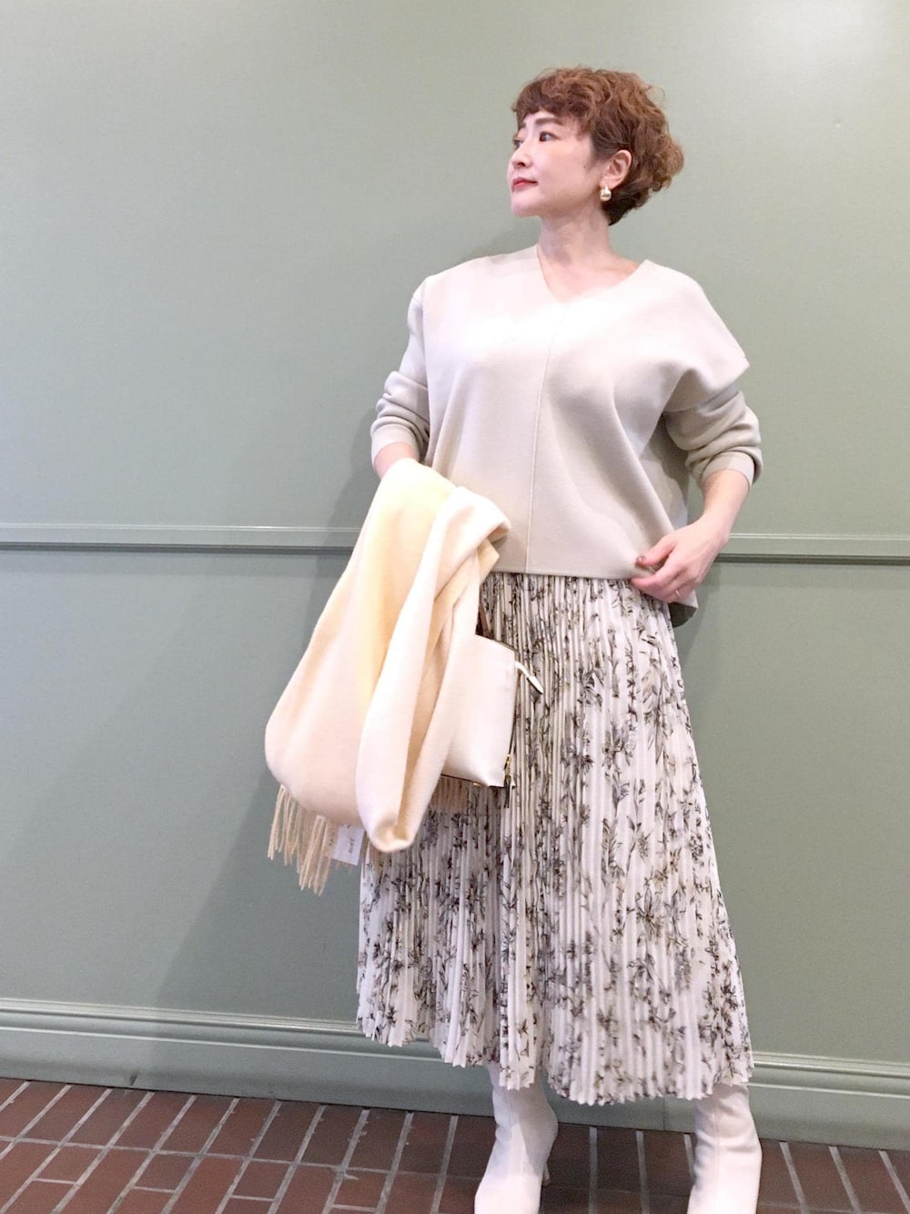 ホワイト系のハンドバッグ、ホワイト系のブーツ、ベージュ系のニット/セーターを着用したレディースの秋コーディネートの1枚目の写真