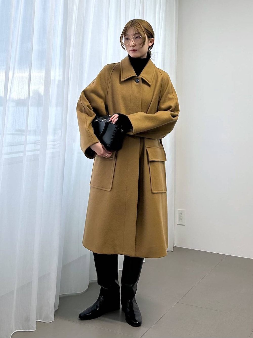 イエロー系のステンカラーコート、ブラック系のボストンバッグ、ブラック系のニット/セーターを着用したレディースの秋コーディネートの1枚目の写真