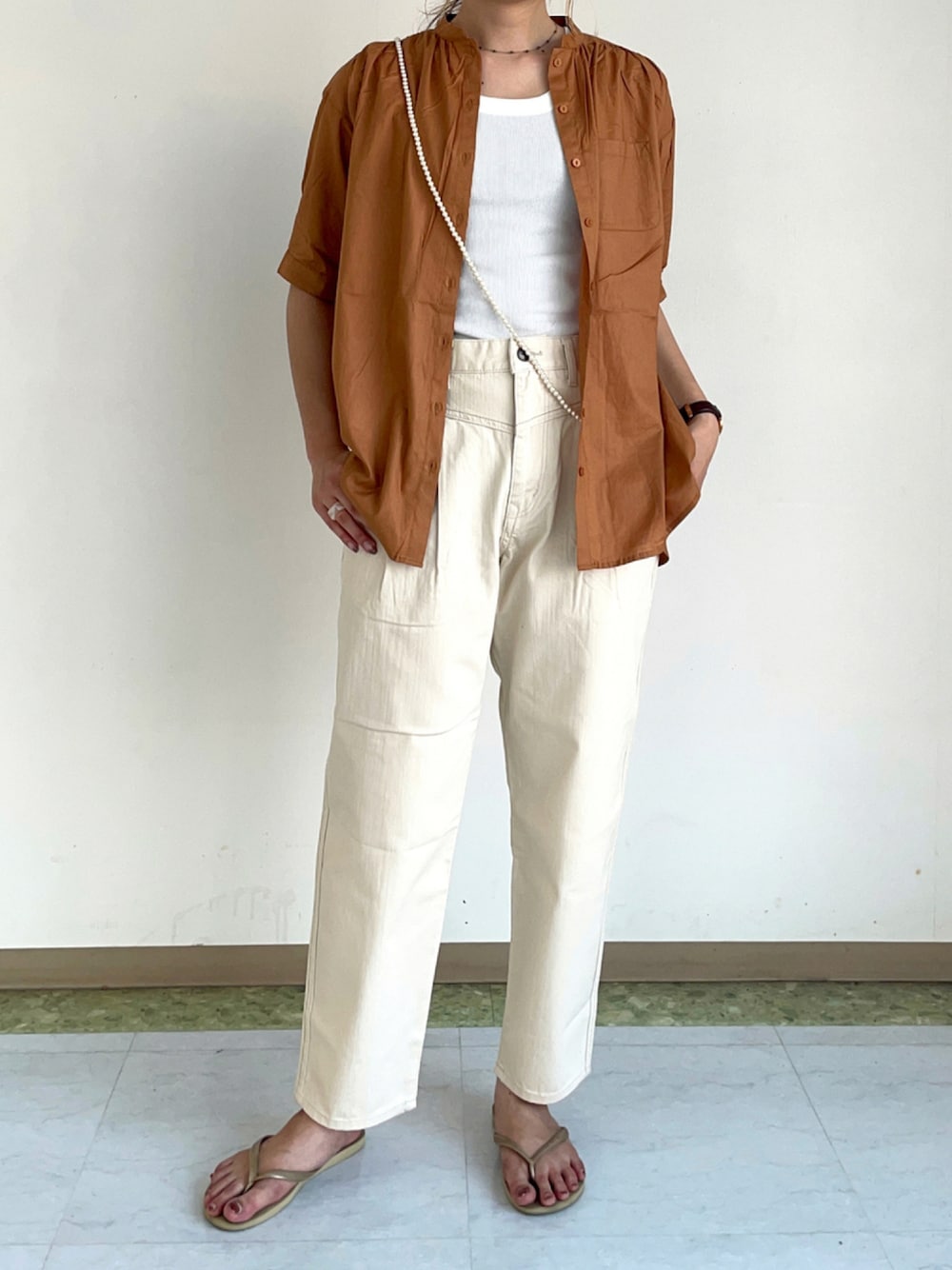 ホワイト系のタンクトップ、ベージュ系のデニムパンツ、ベージュ系のビーチサンダルを着用したレディースの秋コーディネートの1枚目の写真