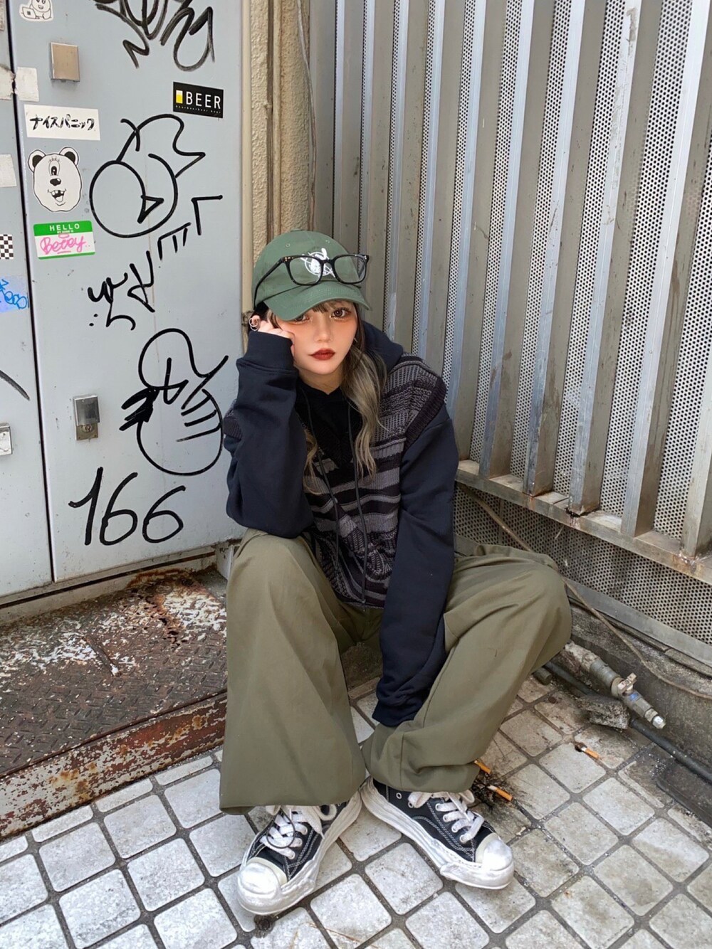 ブラック系のベスト、グリーン系のキャップ、ブラック系のメガネを着用したレディースの冬コーディネートの1枚目の写真