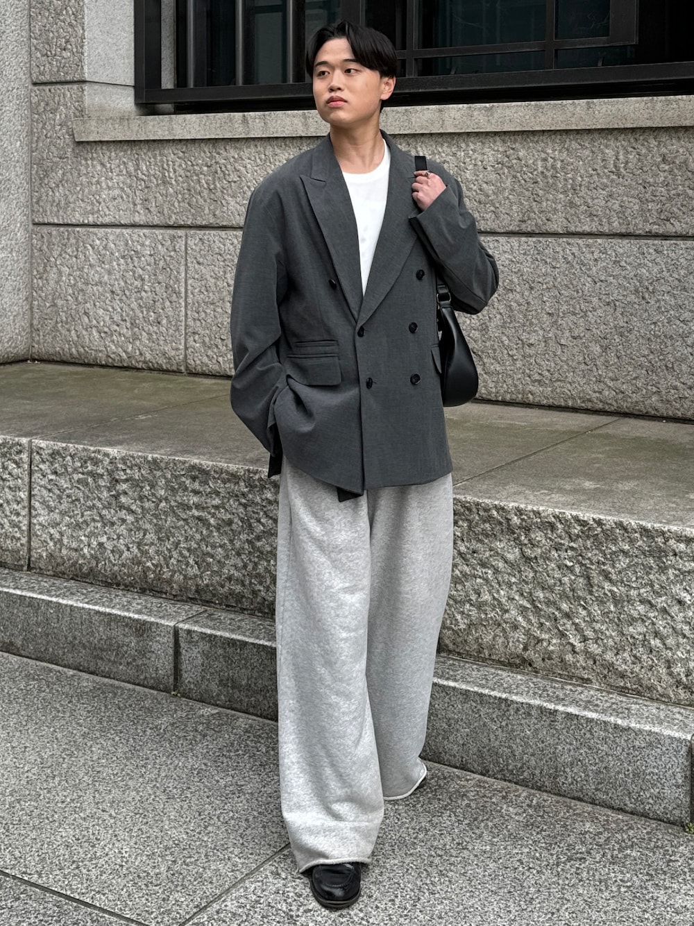 グレー系のテーラードジャケット、ブラック系のショルダーバッグ、グレー系のスウェットパンツを着用したメンズの春コーディネートの1枚目の写真