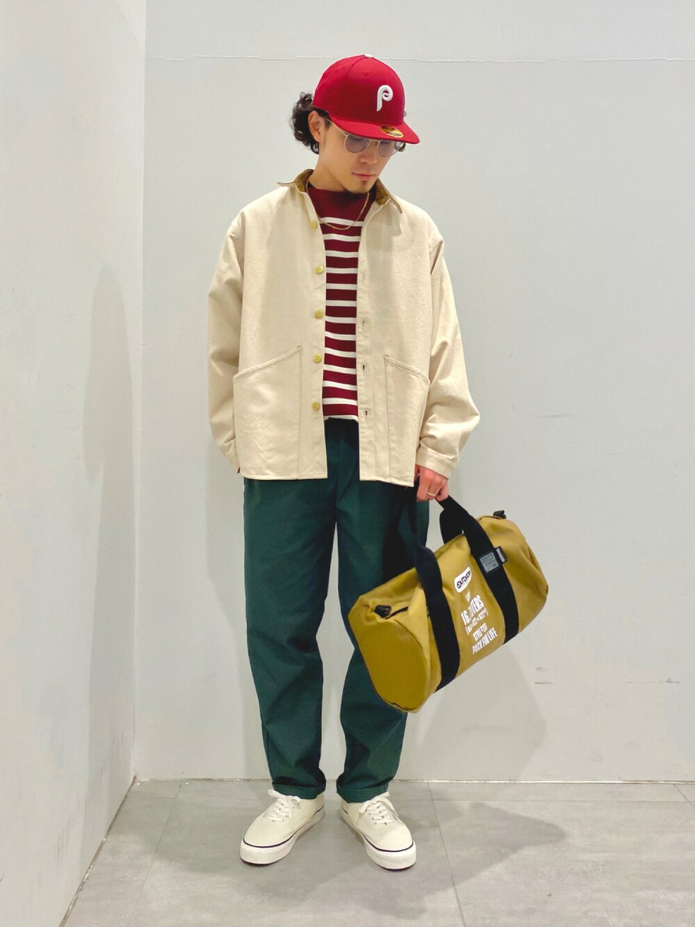 レッド系のTシャツ/カットソー、グリーン系のチノパンツ、ベージュ系のバッグを着用したメンズの秋コーディネートの1枚目の写真
