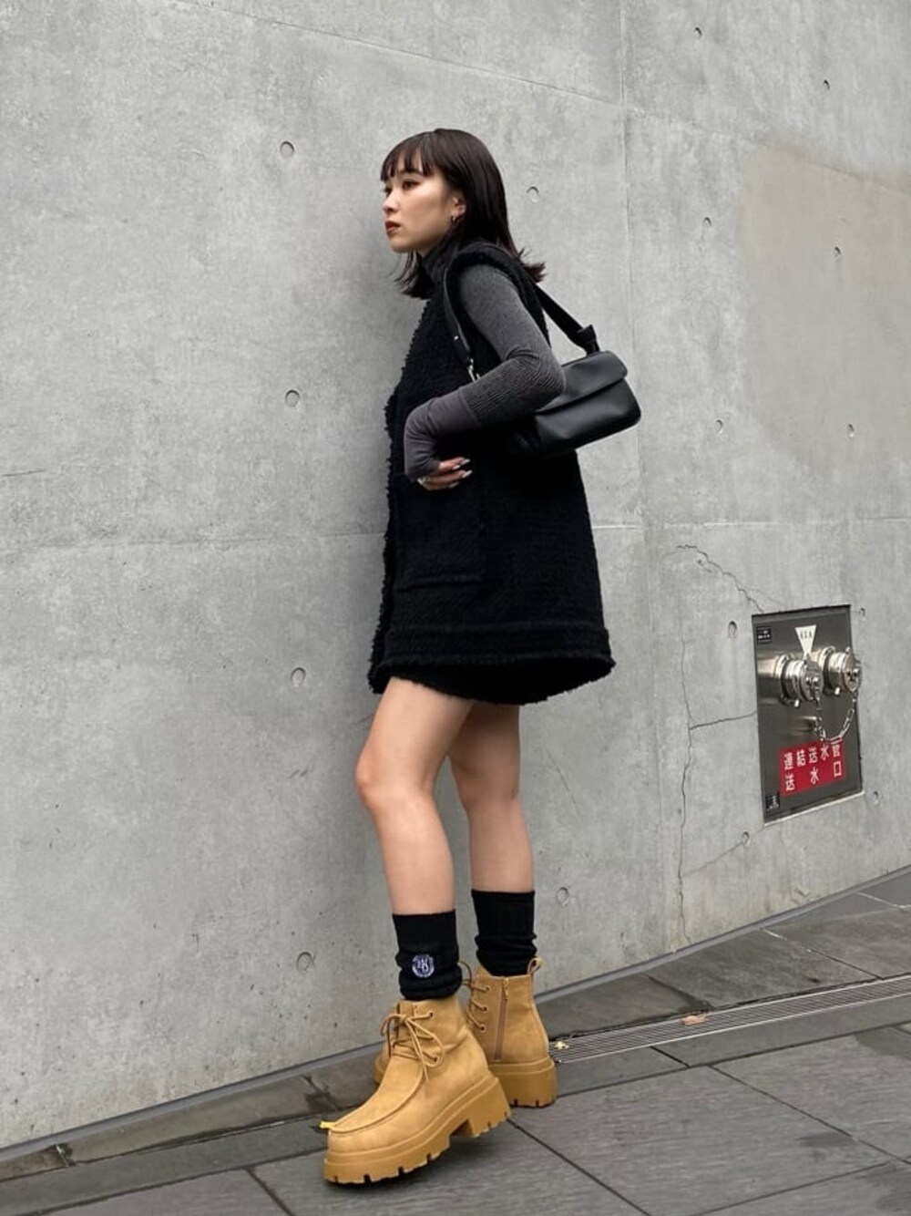 ブラック系のベスト、ブラック系のスカート、ブラウン系のブーツを着用したレディースの夏コーディネートの1枚目の写真