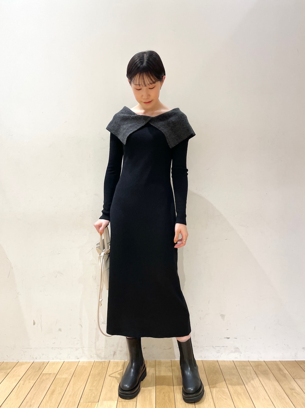 ブラック系のワンピース、ホワイト系のハンドバッグ、ブラック系のブーツを着用したレディースの冬コーディネートの1枚目の写真