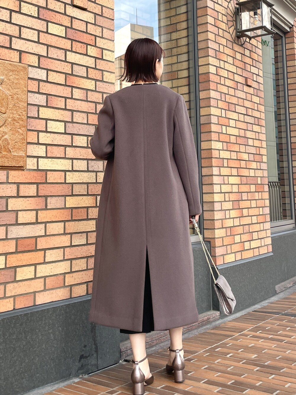 グレー系のノーカラーコート、ブラック系のドレス、シルバー系のハンドバッグを着用したレディースの秋コーディネートの1枚目の写真
