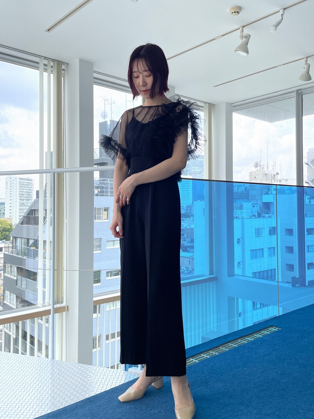 ブラック系のパンツドレス、ベージュ系のパンプスを着用したレディースの春コーディネートの1枚目の写真
