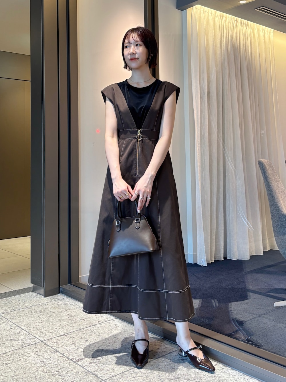 ブラウン系のジャンパースカート、ブラウン系のパンプス、ブラウン系のボストンバッグを着用したレディースの夏コーディネートの1枚目の写真