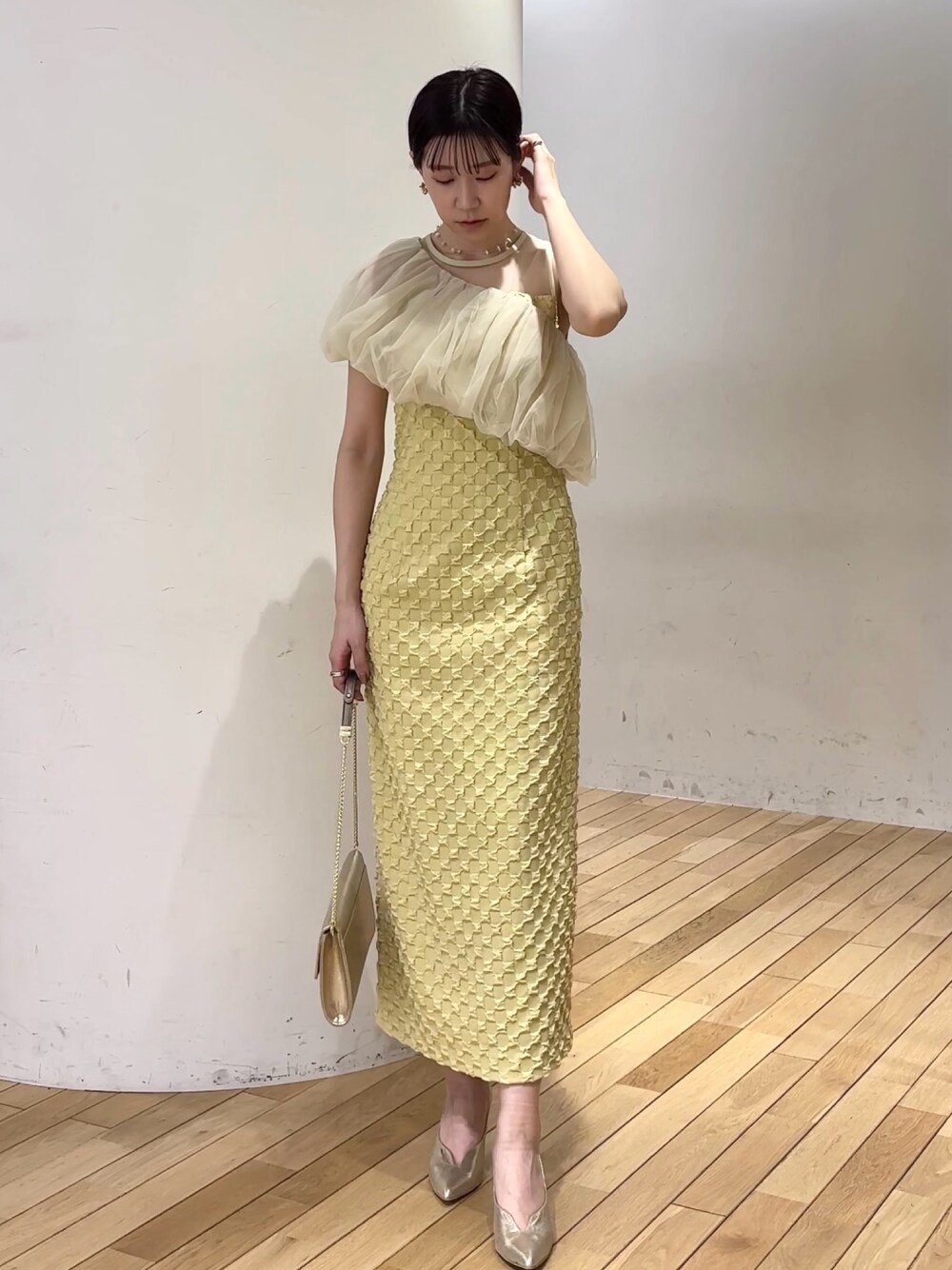 イエロー系のドレス、ゴールド系のパンプス、ゴールド系のクラッチバッグを着用したレディースの春コーディネートの1枚目の写真