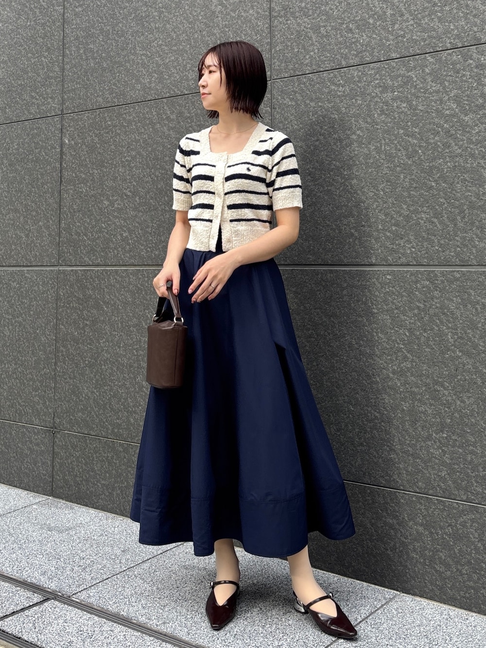 ブルー系のスカート、ホワイト系のニット/セーター、ブラウン系のハンドバッグを着用したレディースの春コーディネートの1枚目の写真