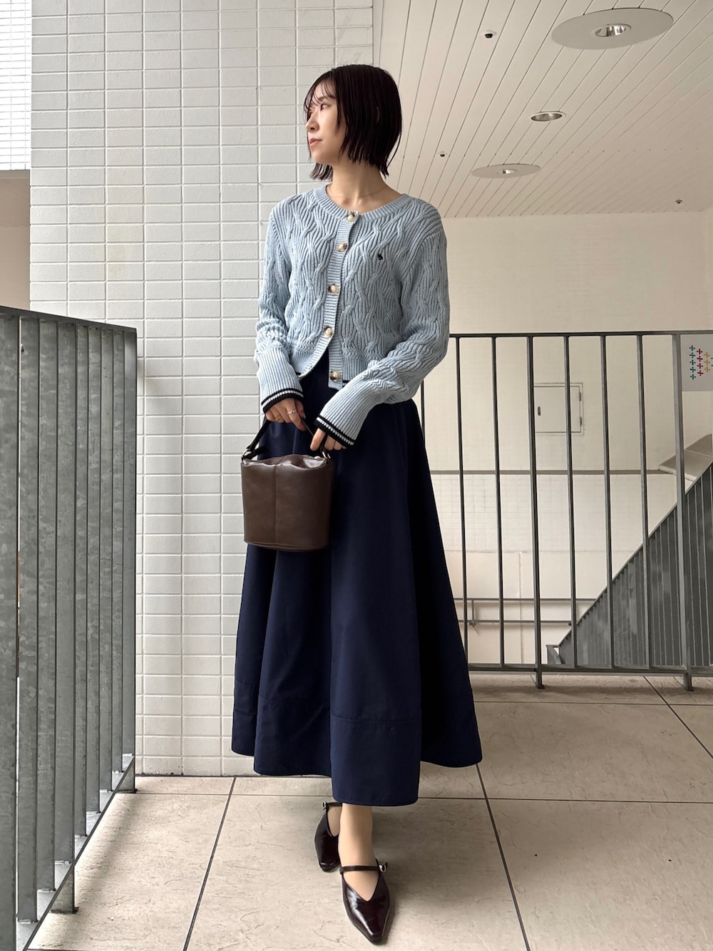 ブルー系のスカート、ブルー系のワンピース、ブラウン系のハンドバッグを着用したレディースの春コーディネートの1枚目の写真