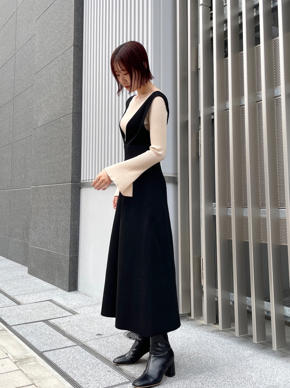 ホワイト系のニット/セーター、ブラック系のジャンパースカート、ブラック系のブーツを着用したレディースの冬コーディネートの1枚目の写真