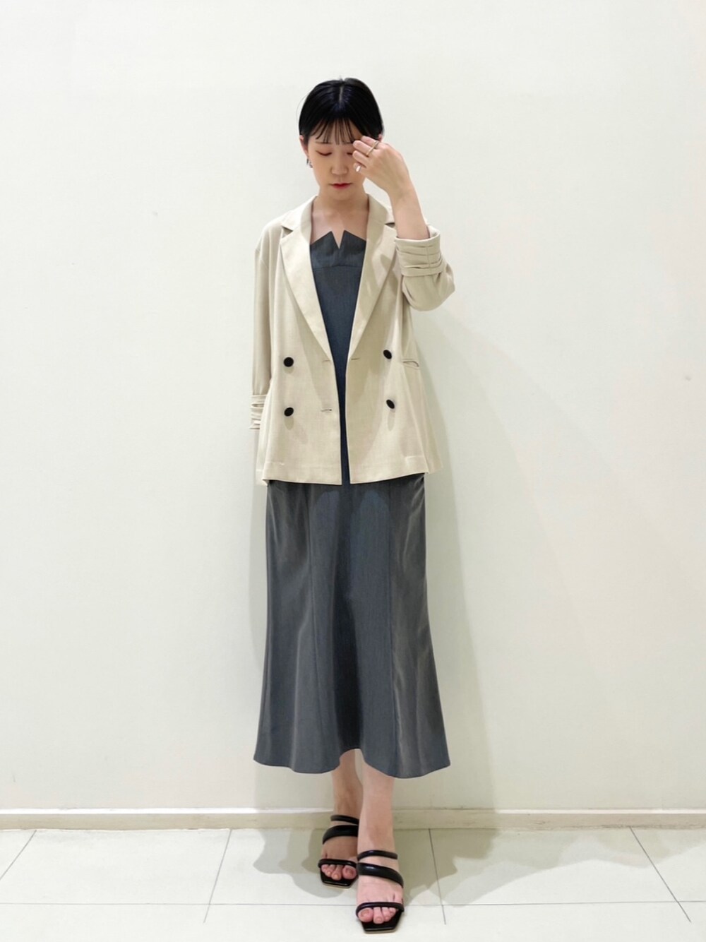 ベージュ系のテーラードジャケット、グレー系のワンピース、ブラック系のサンダルを着用したレディースの春コーディネートの1枚目の写真