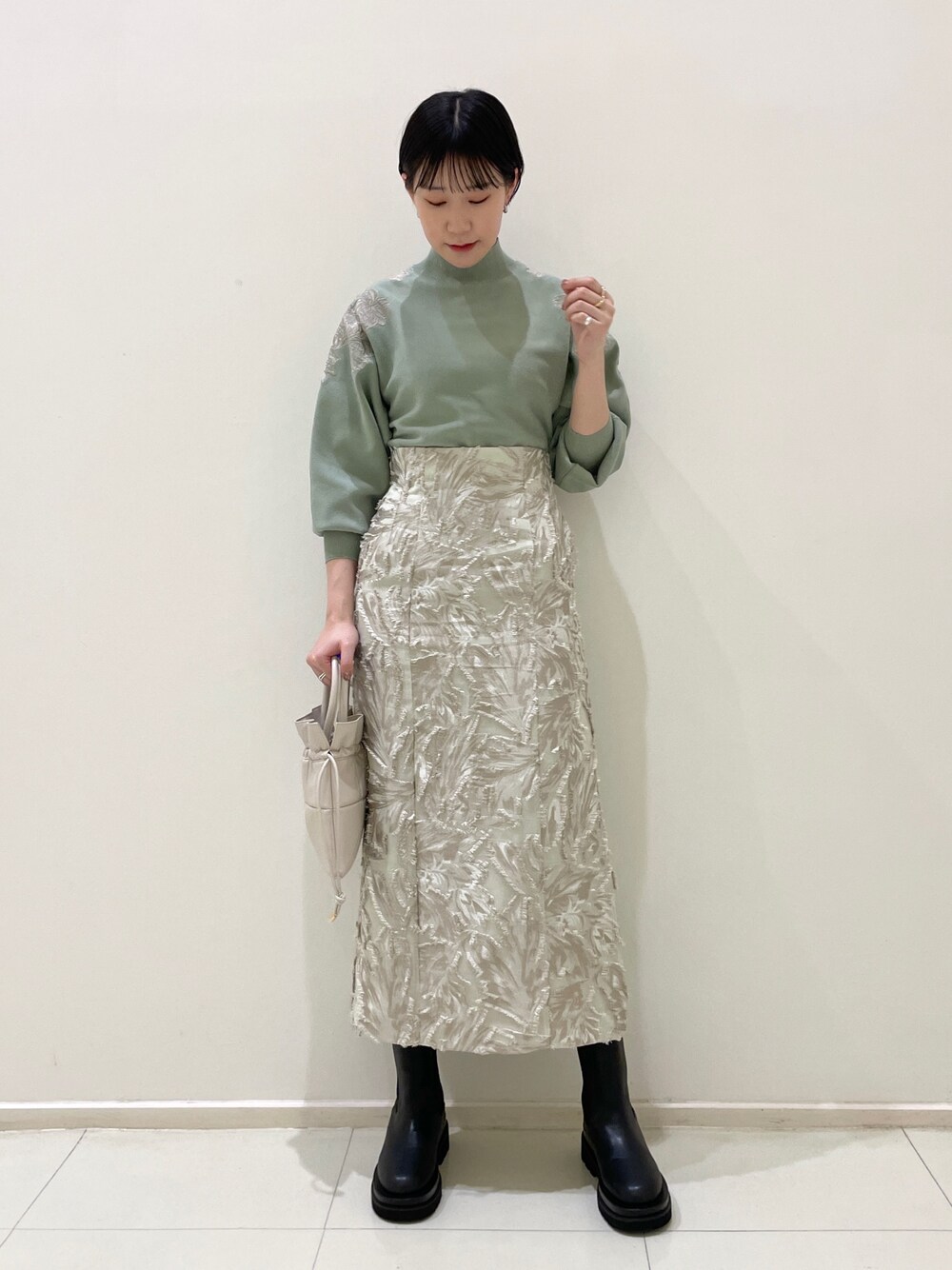 ベージュ系のスカート、グリーン系のニット/セーター、ホワイト系のハンドバッグを着用したレディースの冬コーディネートの1枚目の写真