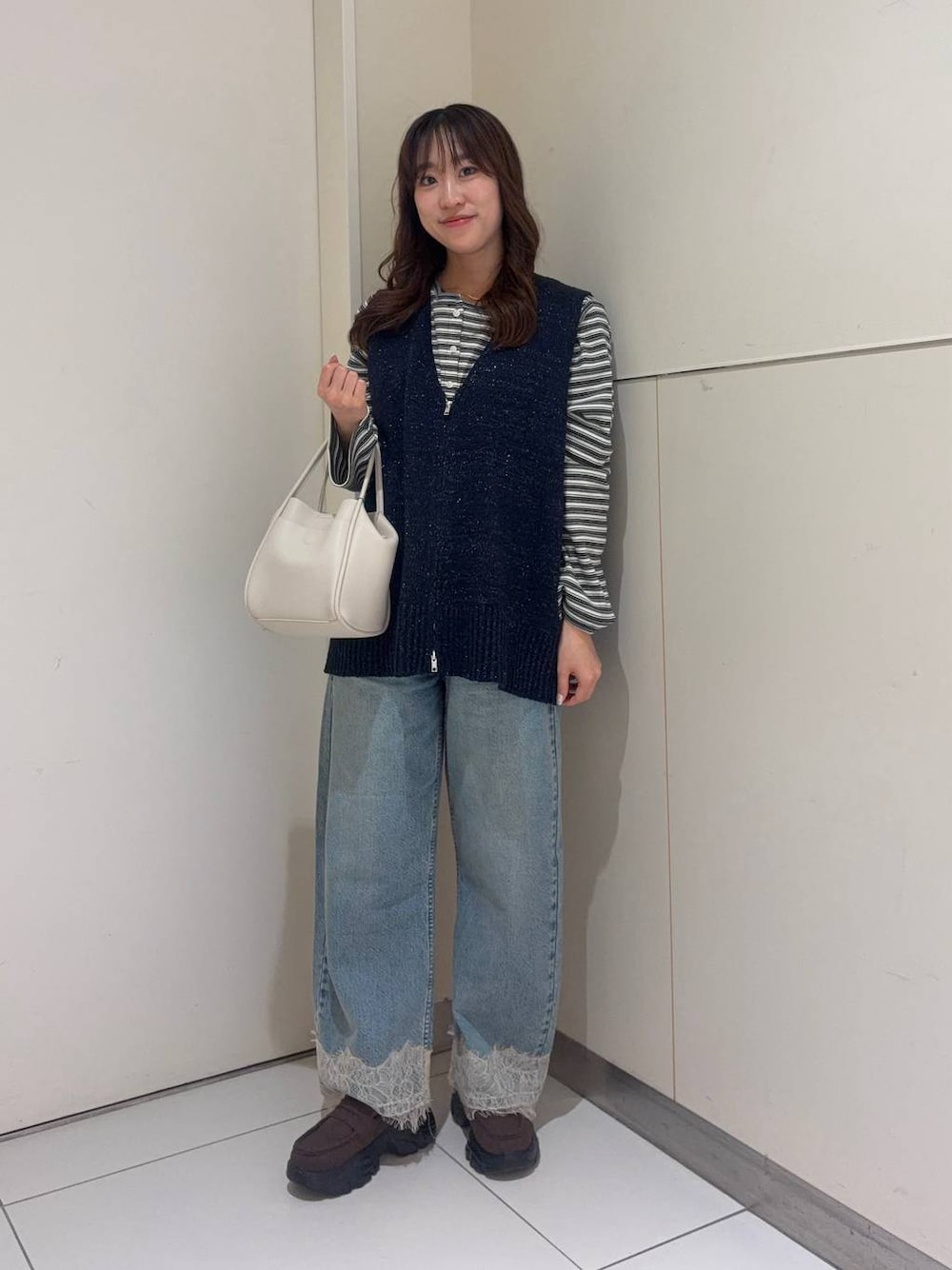 ホワイト系のショルダーバッグ、ブルー系のデニムパンツ、ブラウン系のローファーを着用したレディースの春コーディネートの1枚目の写真