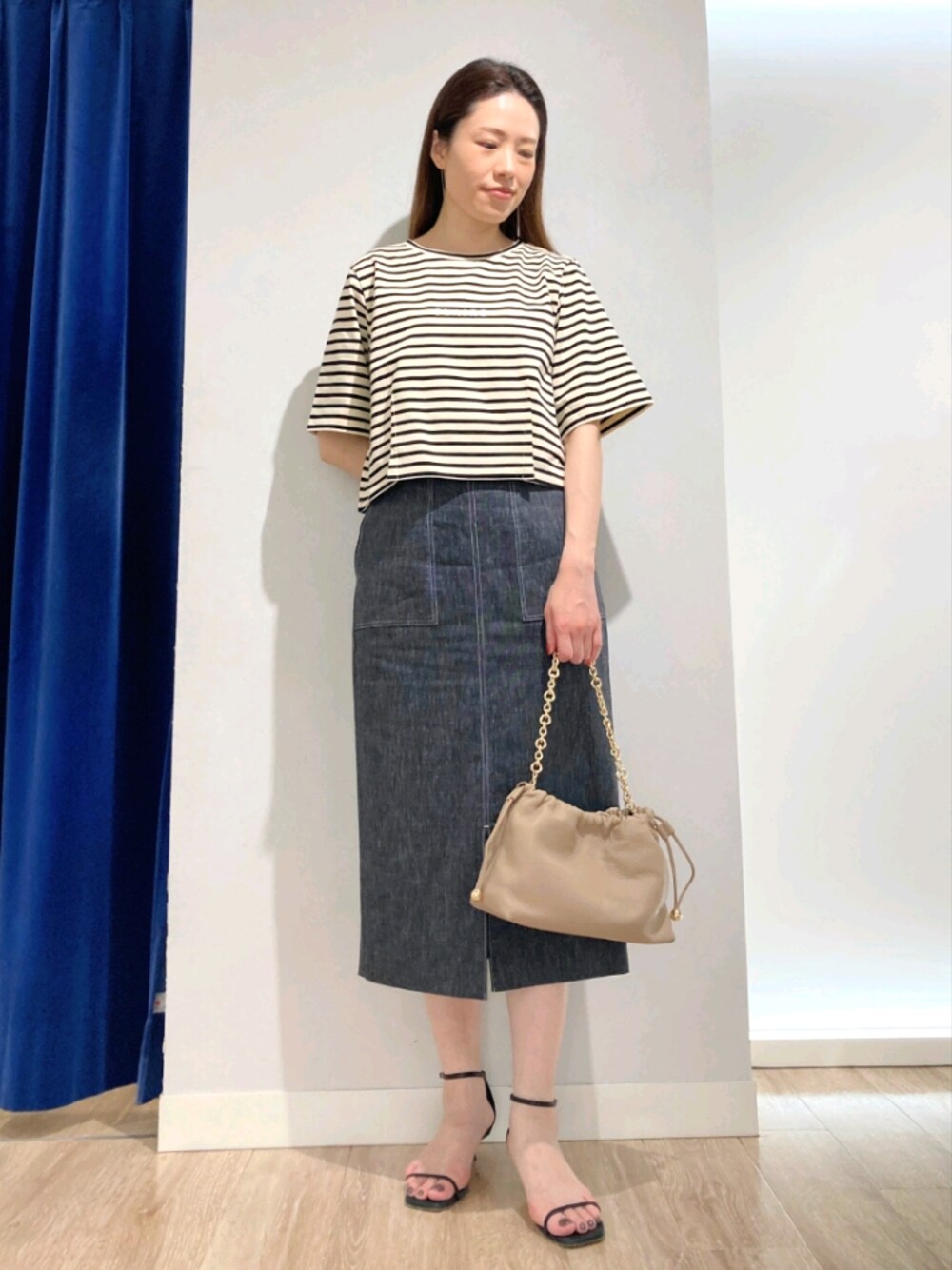 ベージュ系のTシャツ/カットソー、ブルー系のスカート、ベージュ系のショルダーバッグを着用したレディースの夏コーディネートの1枚目の写真