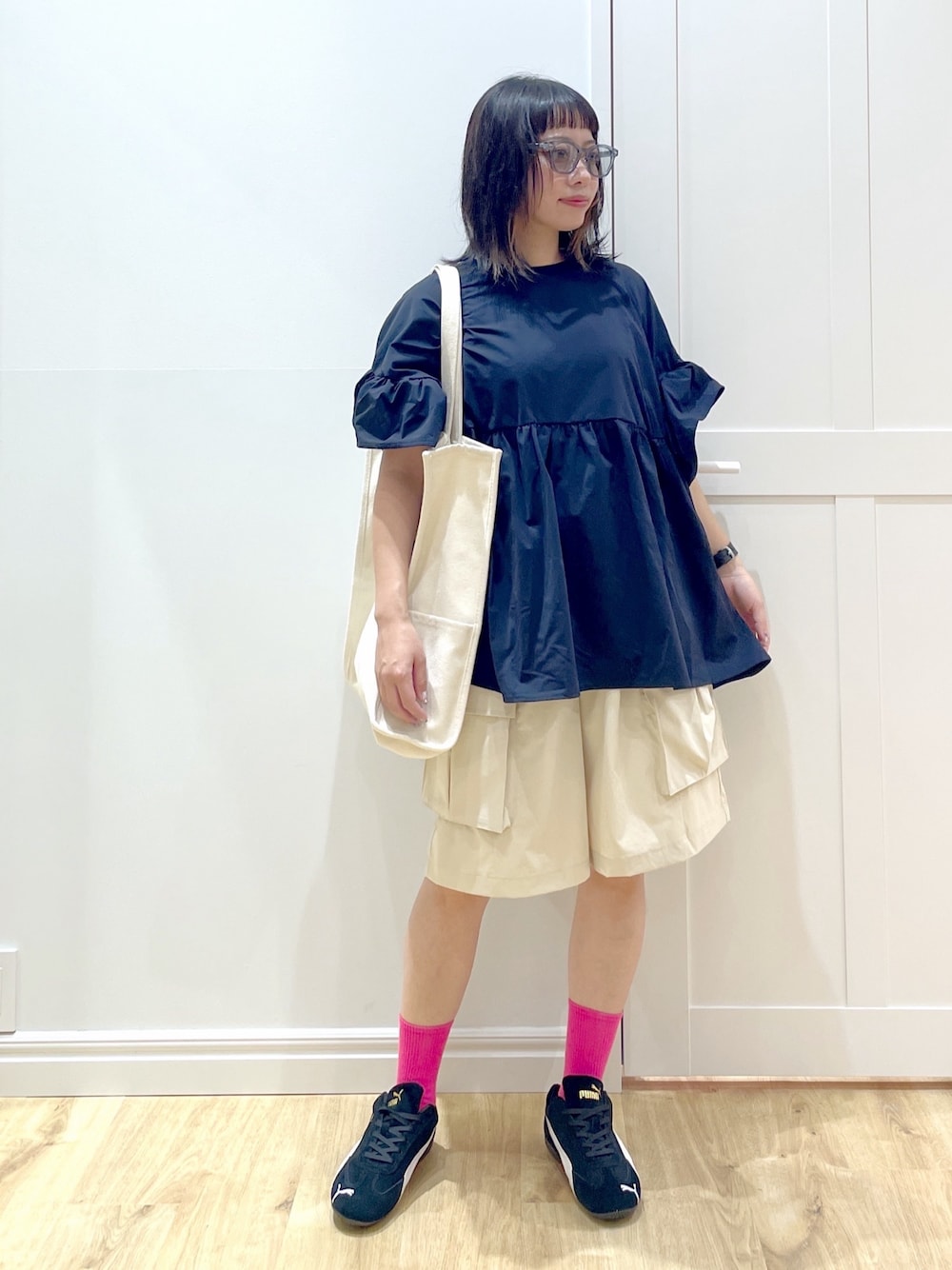 ブラック系のスニーカー、ホワイト系のトートバッグ、ブルー系のサングラスを着用したレディースの夏コーディネートの1枚目の写真