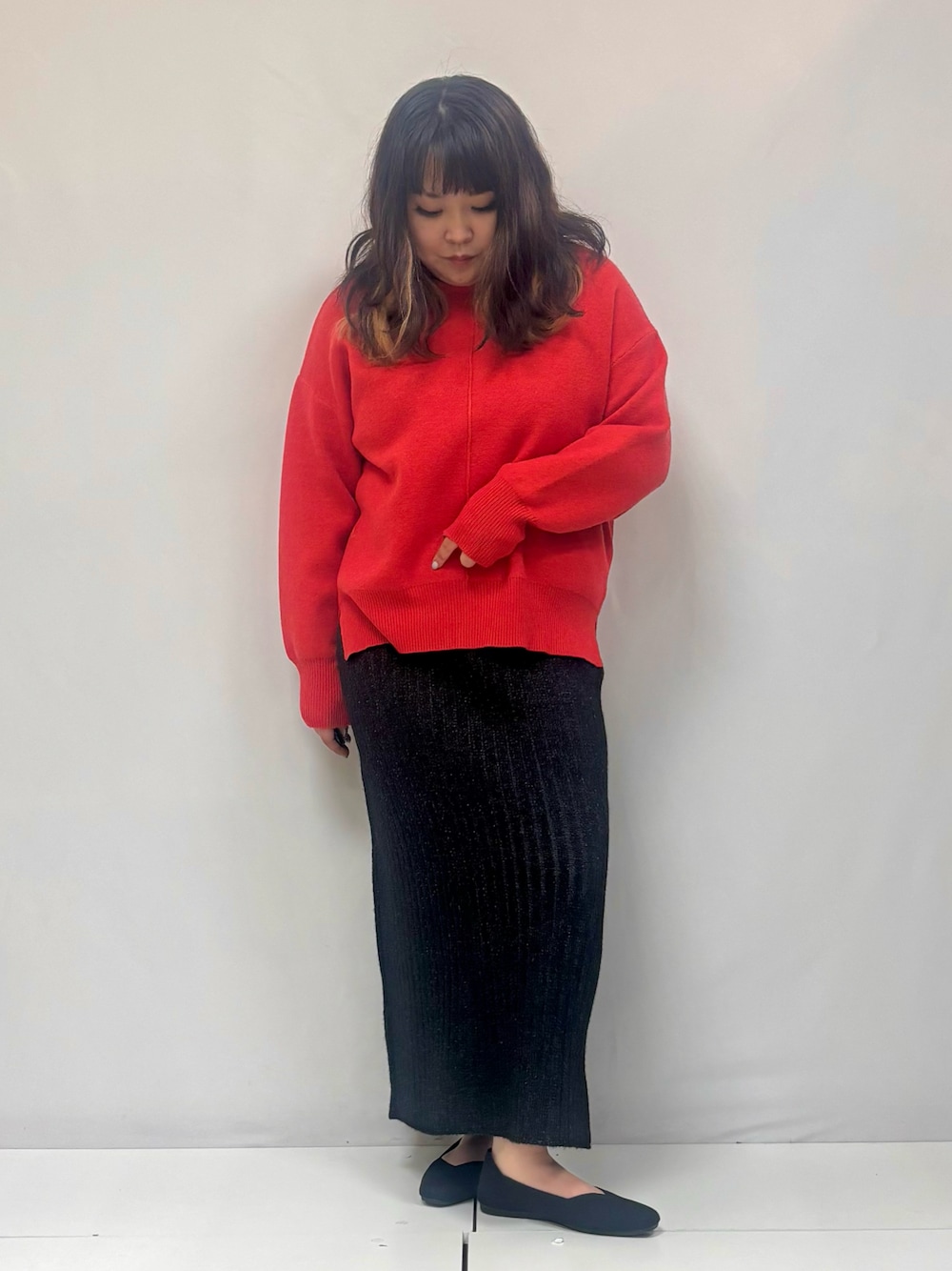 オレンジ系のニット/セーター、ブラック系のスカート、ブラック系のパンプスを着用したレディースの冬コーディネートの1枚目の写真