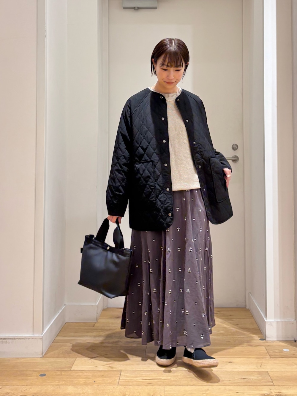 ブラック系のハンドバッグ、グレー系のニット/セーター、グレー系のスカートを着用したレディースの春コーディネートの1枚目の写真