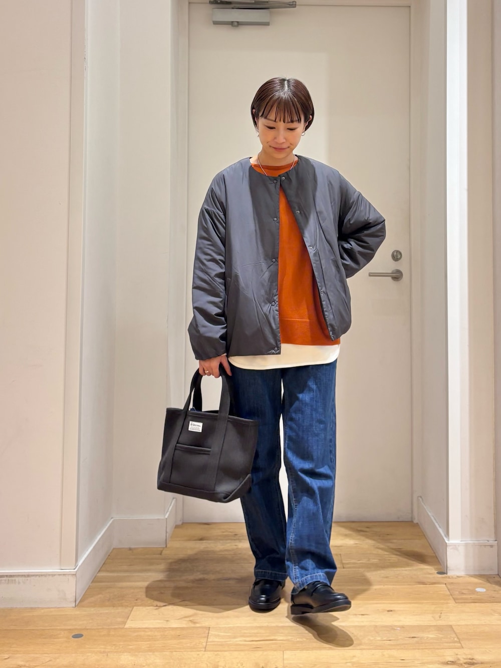 グレー系のブルゾン、オレンジ系のニット/セーター、ホワイト系のTシャツ/カットソーを着用したレディースの秋コーディネートの1枚目の写真