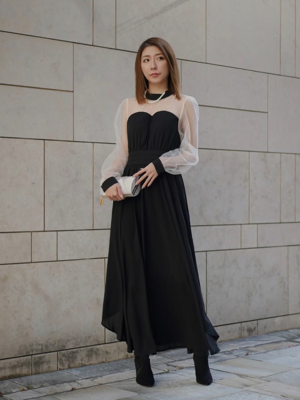 ブラック系のドレス、シルバー系のクラッチバッグ、ホワイト系のネックレスを着用したレディースの冬コーディネートの1枚目の写真