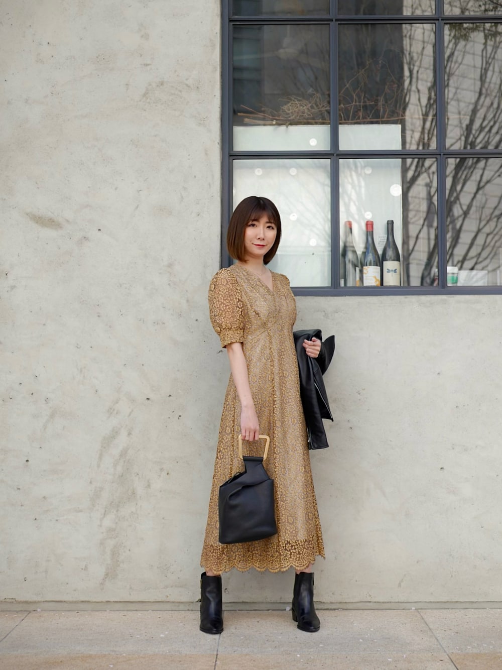 イエロー系のドレス、ブラック系のハンドバッグ、ブラック系のブーツを着用したレディースの春コーディネートの1枚目の写真