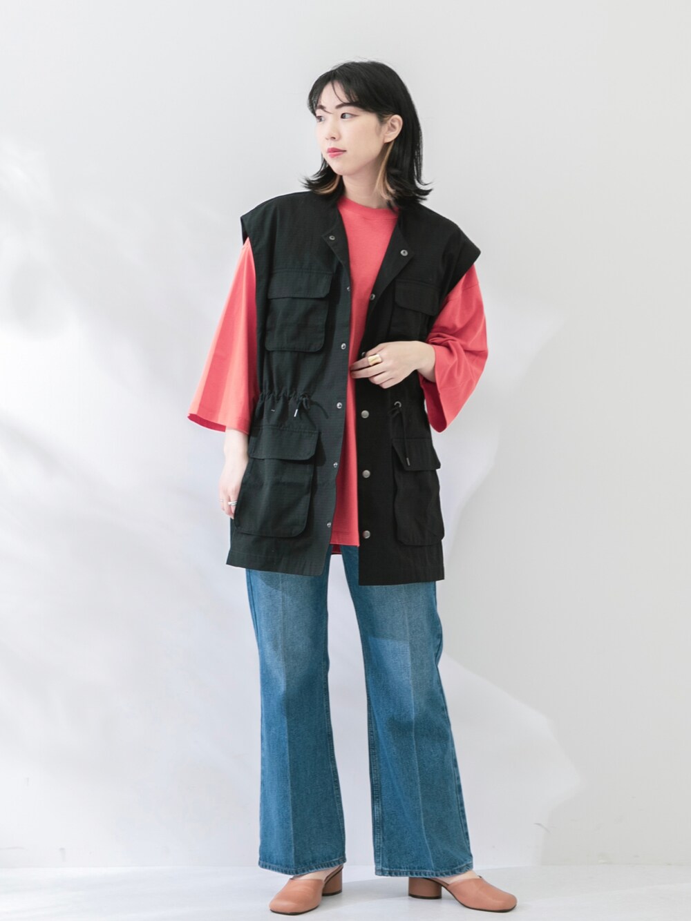 ブラック系のベスト、オレンジ系のTシャツ/カットソー、ブルー系のデニムパンツを着用したレディースの春コーディネートの1枚目の写真