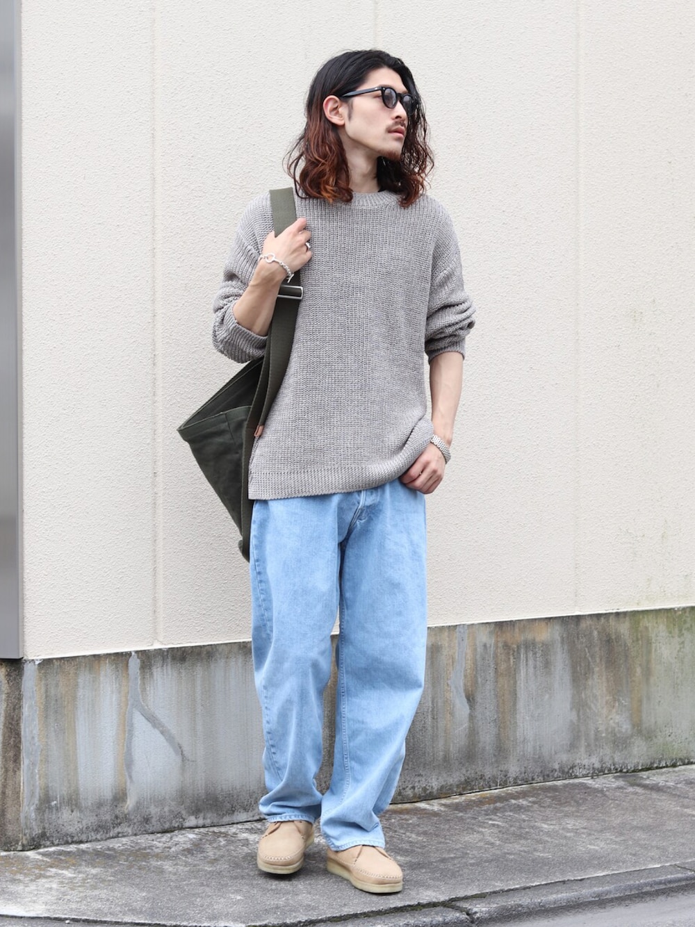 グレー系のニット/セーター、ブルー系のデニムパンツ、グリーン系のショルダーバッグを着用したメンズの夏コーディネートの1枚目の写真